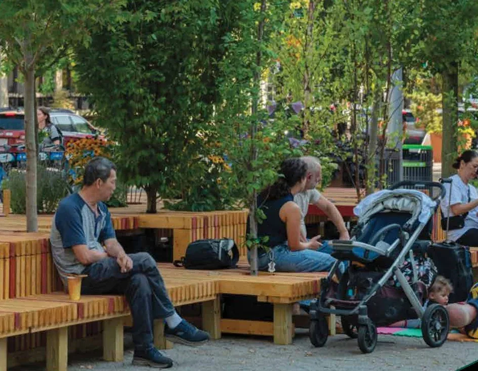 Residents gathering on a wooden parklet under street trees - a small-scale urban intervention showing ambition turned into everyday neighbourhood life.